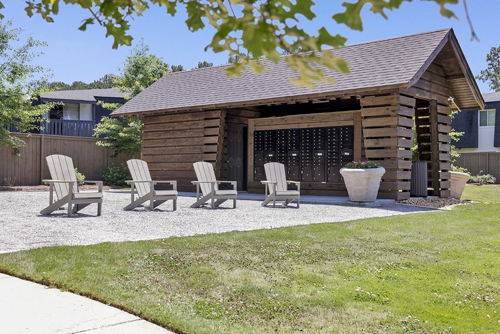 A wooden house with a brown roof and a glass door is surrounded by four chairs and a potted plant.